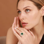 Woman wearing a ring with a green gemstone against a brown background
