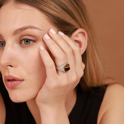 Woman wearing a gemstone signet ring on her finger against a brown background