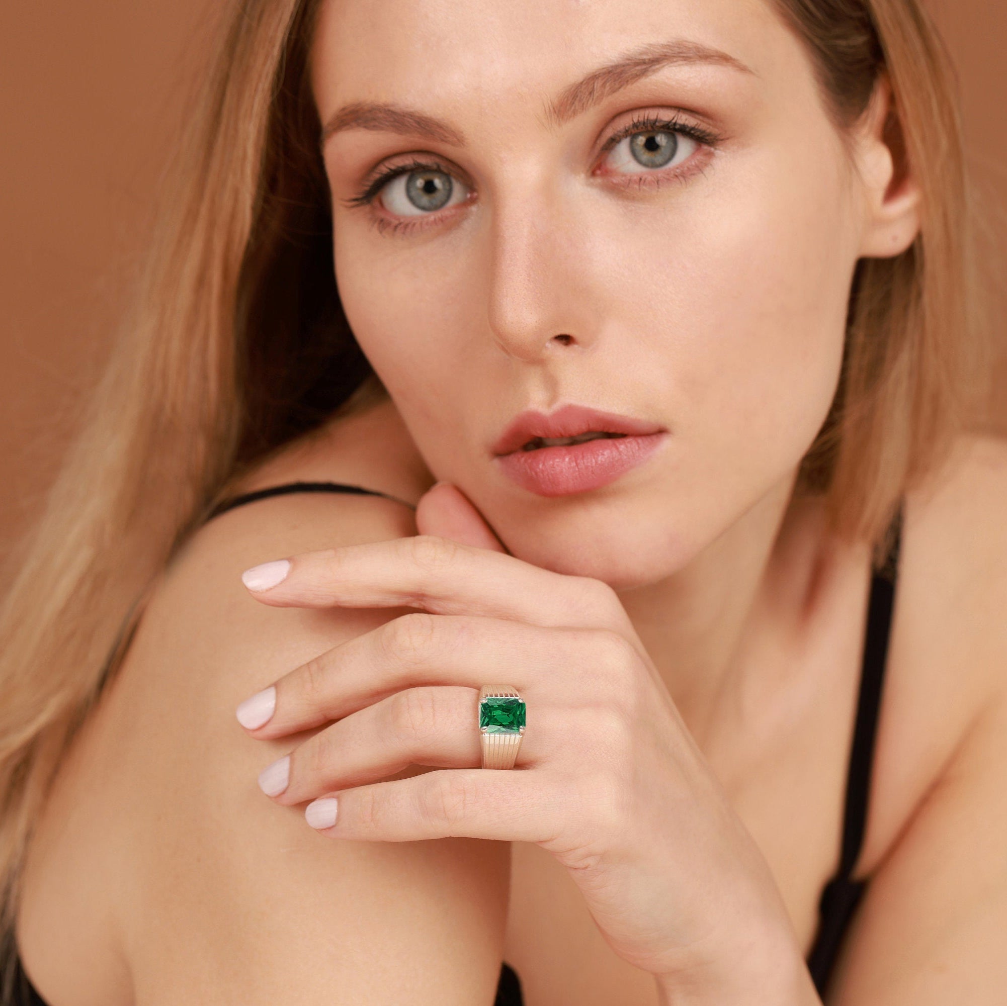 Woman wearing a green gemstone emerald ring on a brown background