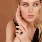 Woman with blonde hair wearing a statement ring against a brown background