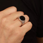 Hand wearing a silver statement ring with a black flat stone on a dark background
