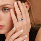 Woman wearing a ring with a square-cut blue gemstone on a brown background