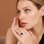 Woman wearing a ring with a blue sapphire gemstone against a brown background