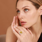 Woman wearing a ring with a yellow gemstone against a brown background