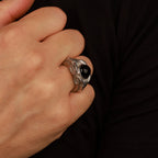 Hand wearing a silver ring with a black stone on a dark background