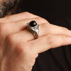 Hand wearing a silver ring with a black gemstone against a dark background