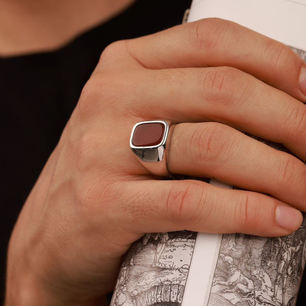 A hand wearing a carnelian ring holding a cylindrical object with a map design.