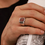 A hand wearing a carnelian ring holding a cylindrical object with a map design.
