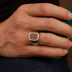 Hand holding a teal mug with a polished signet ring on the finger against a blurred background