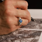 Hand with a skull ring with blue gemstone holding a pen over an engraved sheet of paper