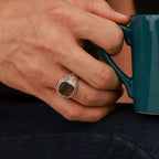 Hand holding a teal mug with a tiger's eye ring