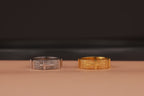 Two rings, one silver and one gold, on a brown surface with a dark background.