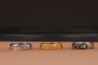 Three rings in silver, gold, and oxidized on a brown surface with a dark background
