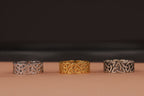 Three rings with Celtic knot designs on a brown surface and dark background