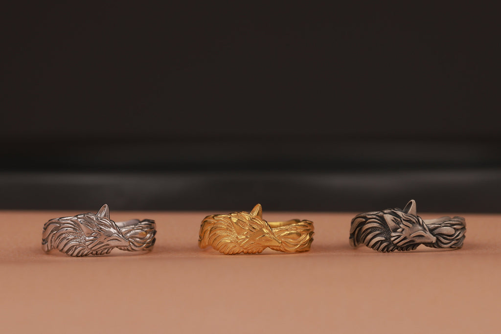 Three metallic rings in silver, gold, and bronze on a brown surface with a dark background