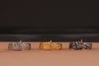 Three metallic rings in silver, gold, and bronze on a brown surface with a dark background