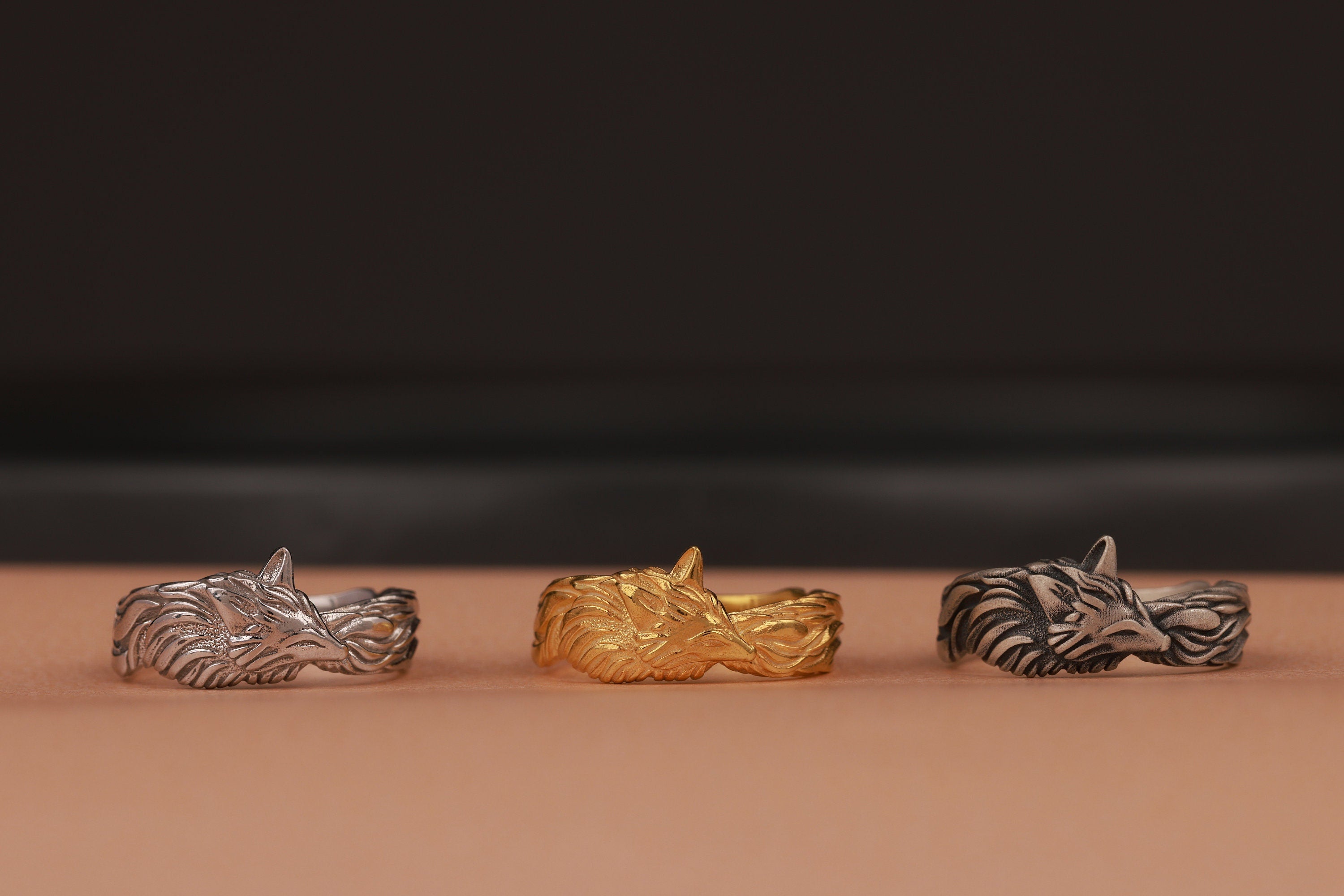 Three metallic rings in silver, gold, and bronze on a brown surface with a dark background