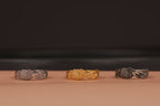 Three rings, two silver and one gold, on a brown surface with a dark background
