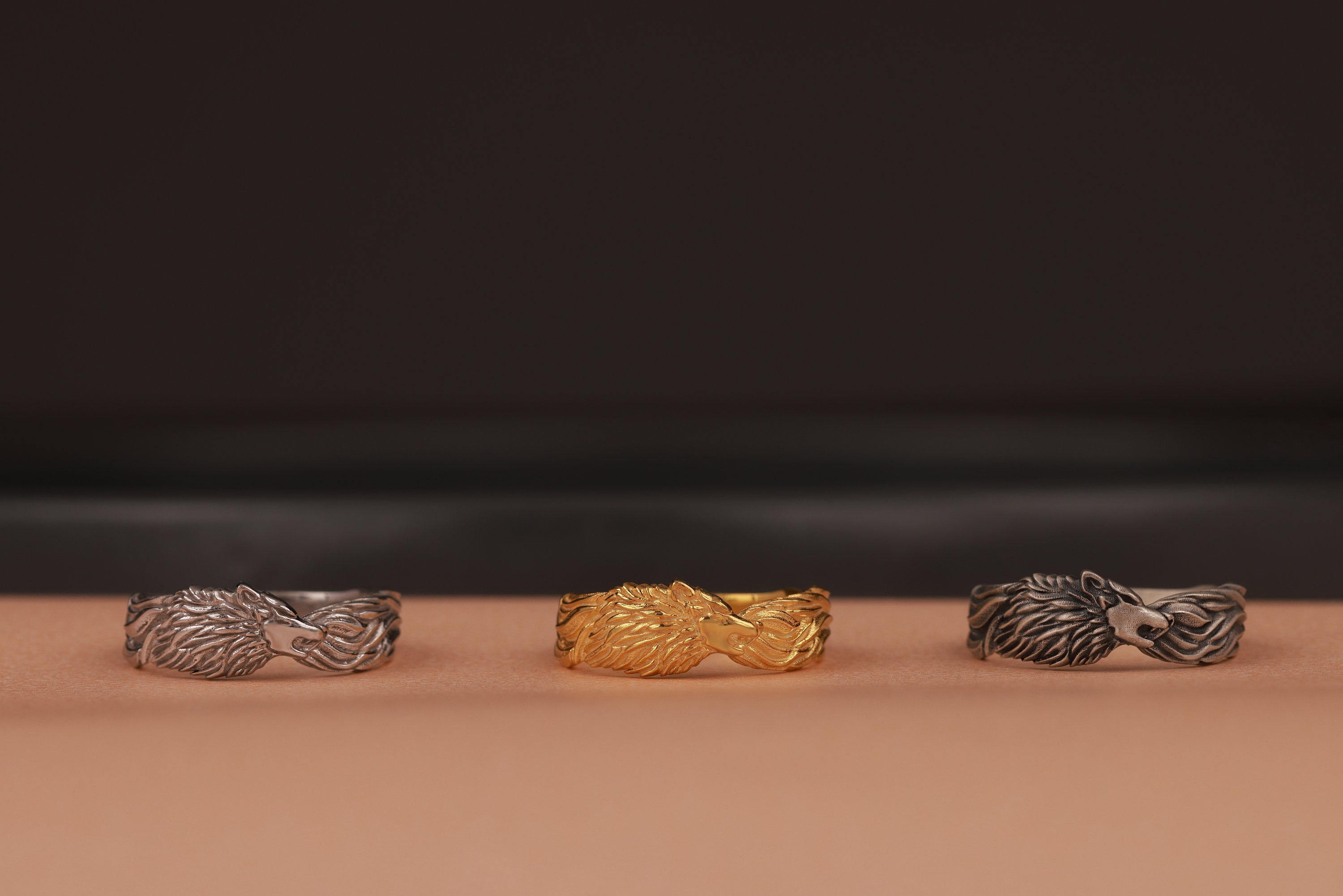 Three rings, two silver and one gold, on a brown surface with a dark background