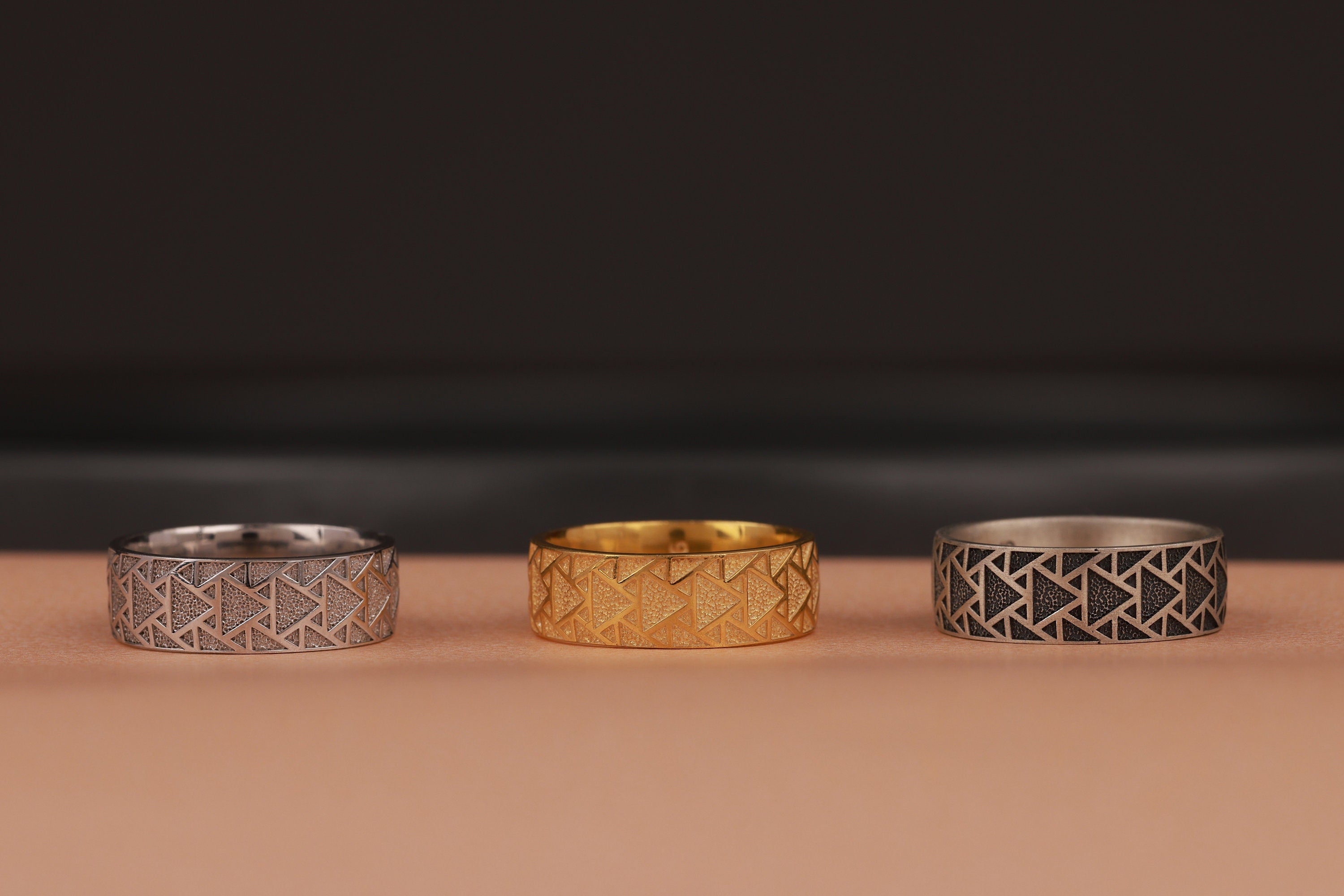 Three rings with geometric patterns on a brown surface and a dark background