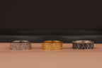 Three band rings, two silver and one gold, on a dark background