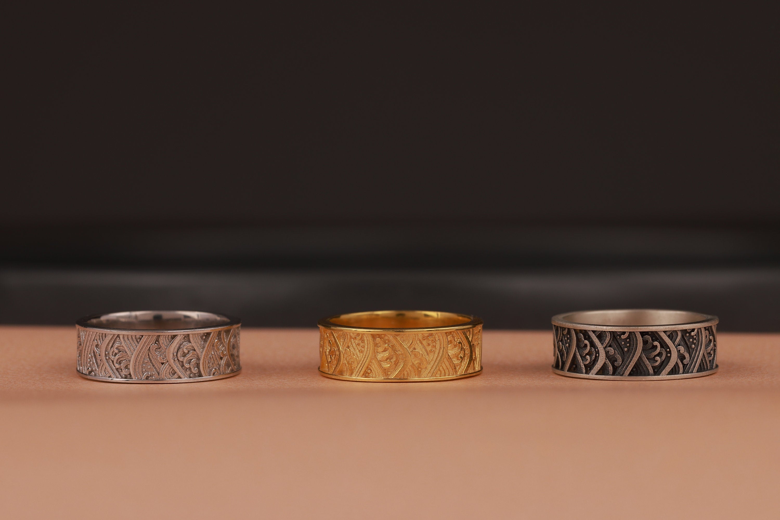 Three band rings, two silver and one gold, on a dark background