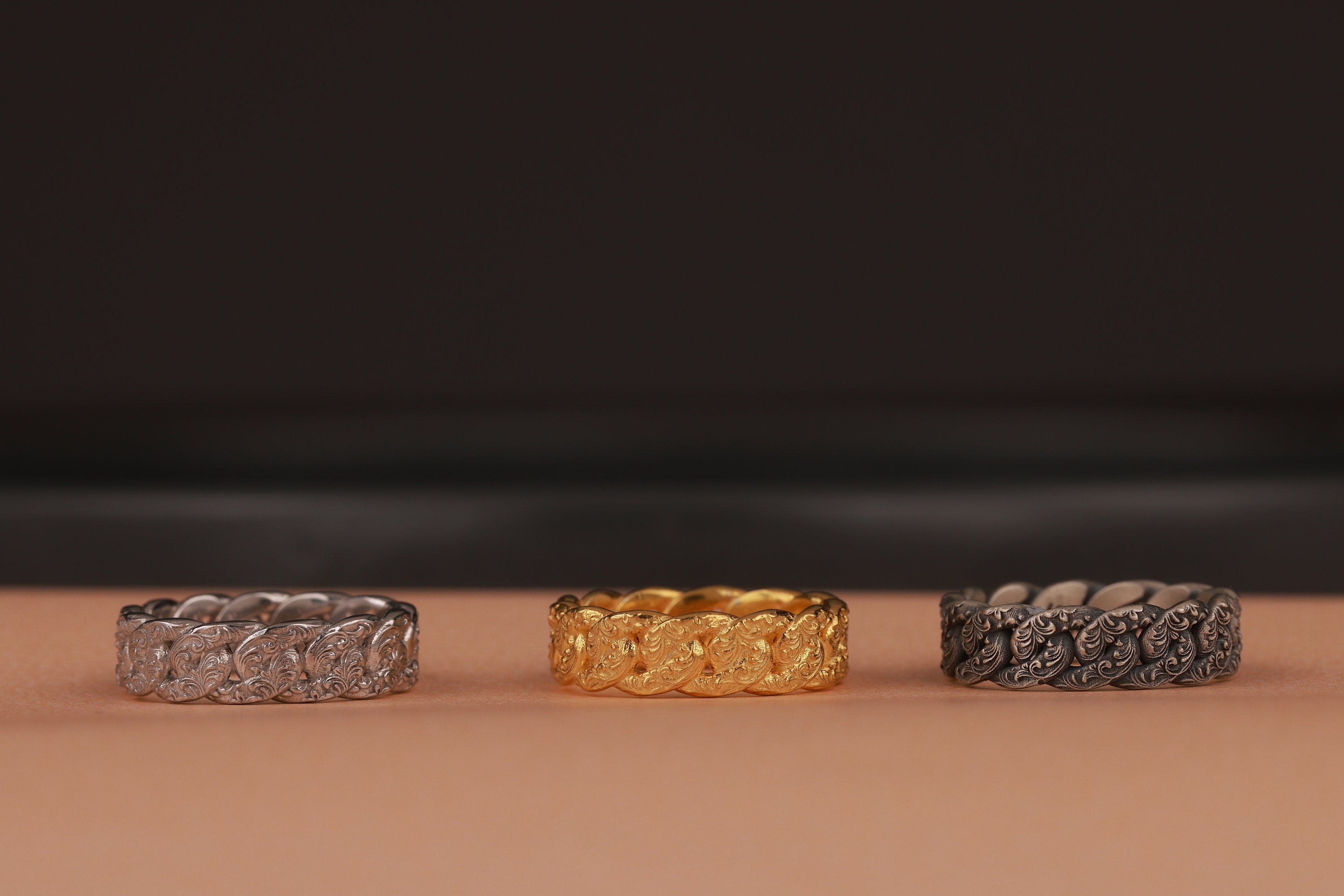 Three rings, two silver and one gold, on a brown surface with a dark background