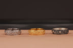 Three rings, two silver and one gold, on a beige surface with a blurred dark background