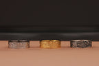 Three rings in silver, gold, and another silver color on a brown surface with a dark background.
