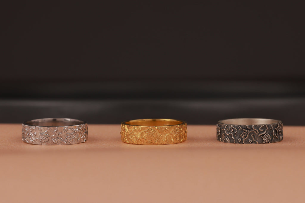 Three rings in silver, gold, and black on a brown surface with a dark background