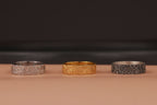 Three rings in silver, gold, and black on a brown surface with a dark background