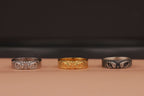 Three rings, two silver and one gold, on a beige surface with a dark background