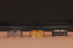 Three rings, two silver and one gold, on a brown surface with a dark background