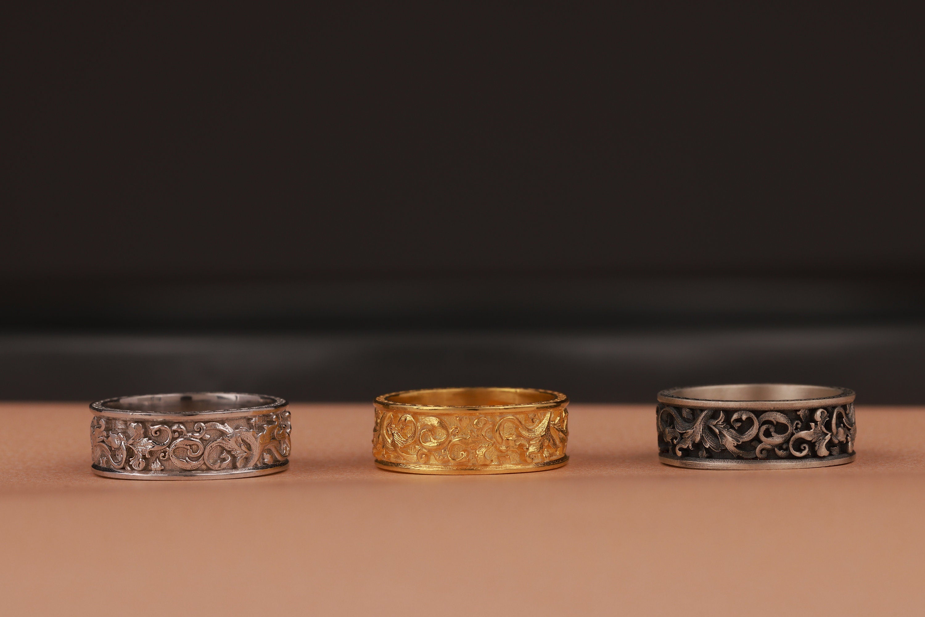Three rings, two silver and one gold, on a brown surface with a dark background