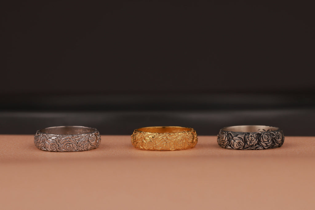 Three rose flower rings, two silver and one gold, on a brown surface with a dark background