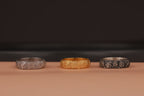 Three rose flower rings, two silver and one gold, on a brown surface with a dark background