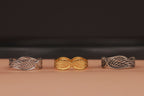 Three variations of angel wings rings with leaf designs on a brown surface and a dark background