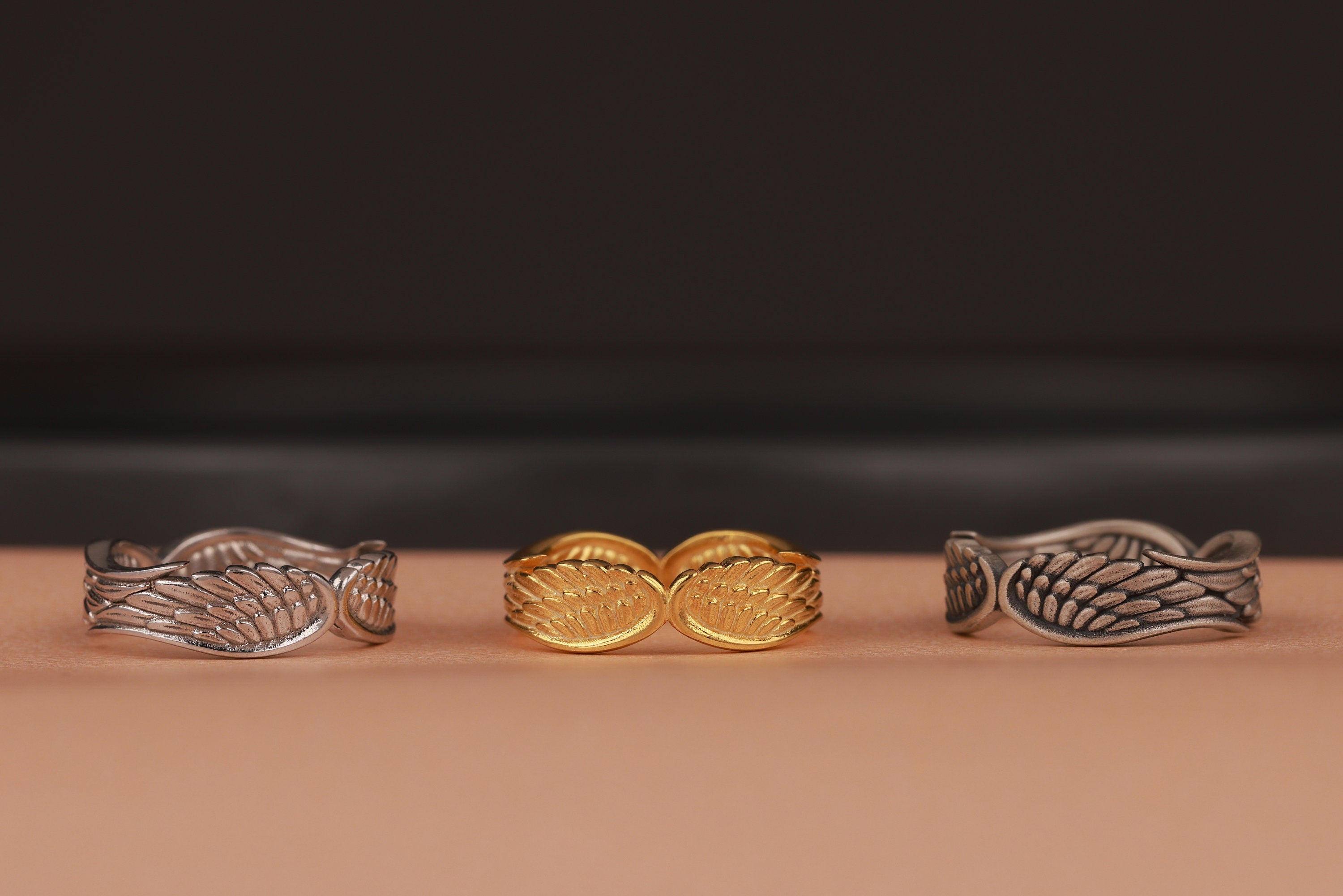 Three variations of angel wings rings with leaf designs on a brown surface and a dark background