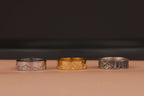 Three nature rings, two silver and one gold, on a brown surface with a dark background