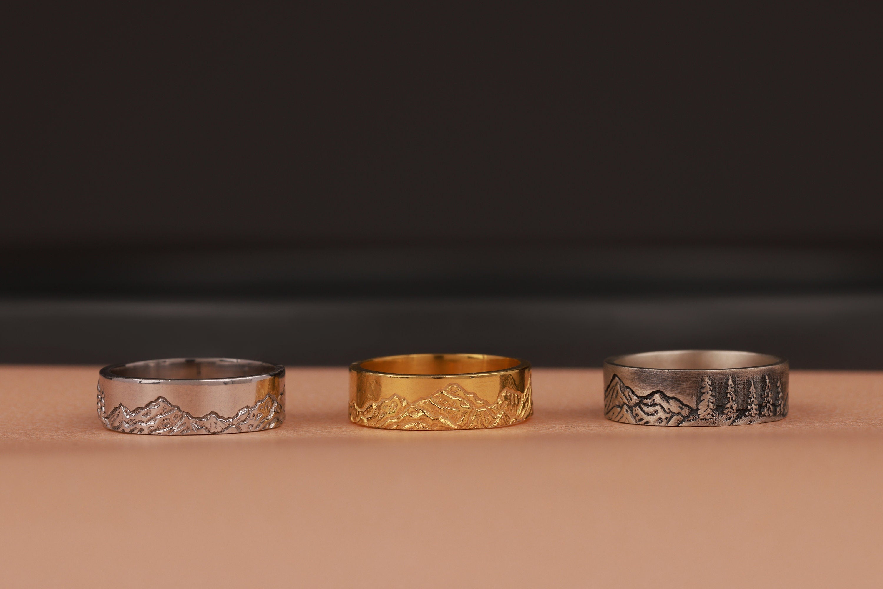 Three nature rings, two silver and one gold, on a brown surface with a dark background