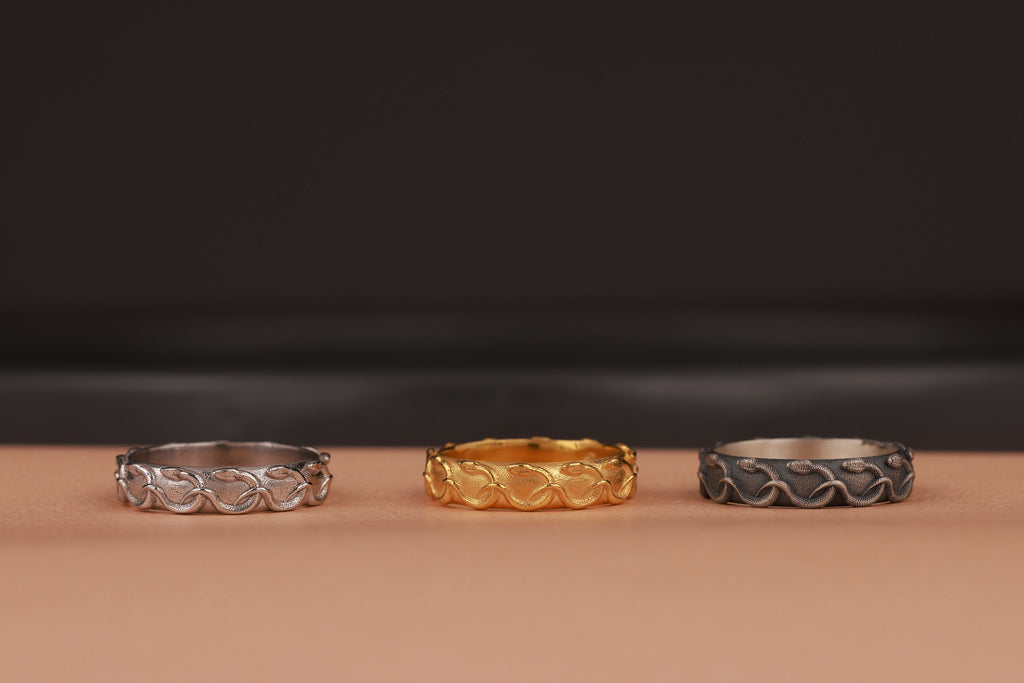 Three rings in silver, gold, and black on a brown surface with a dark background