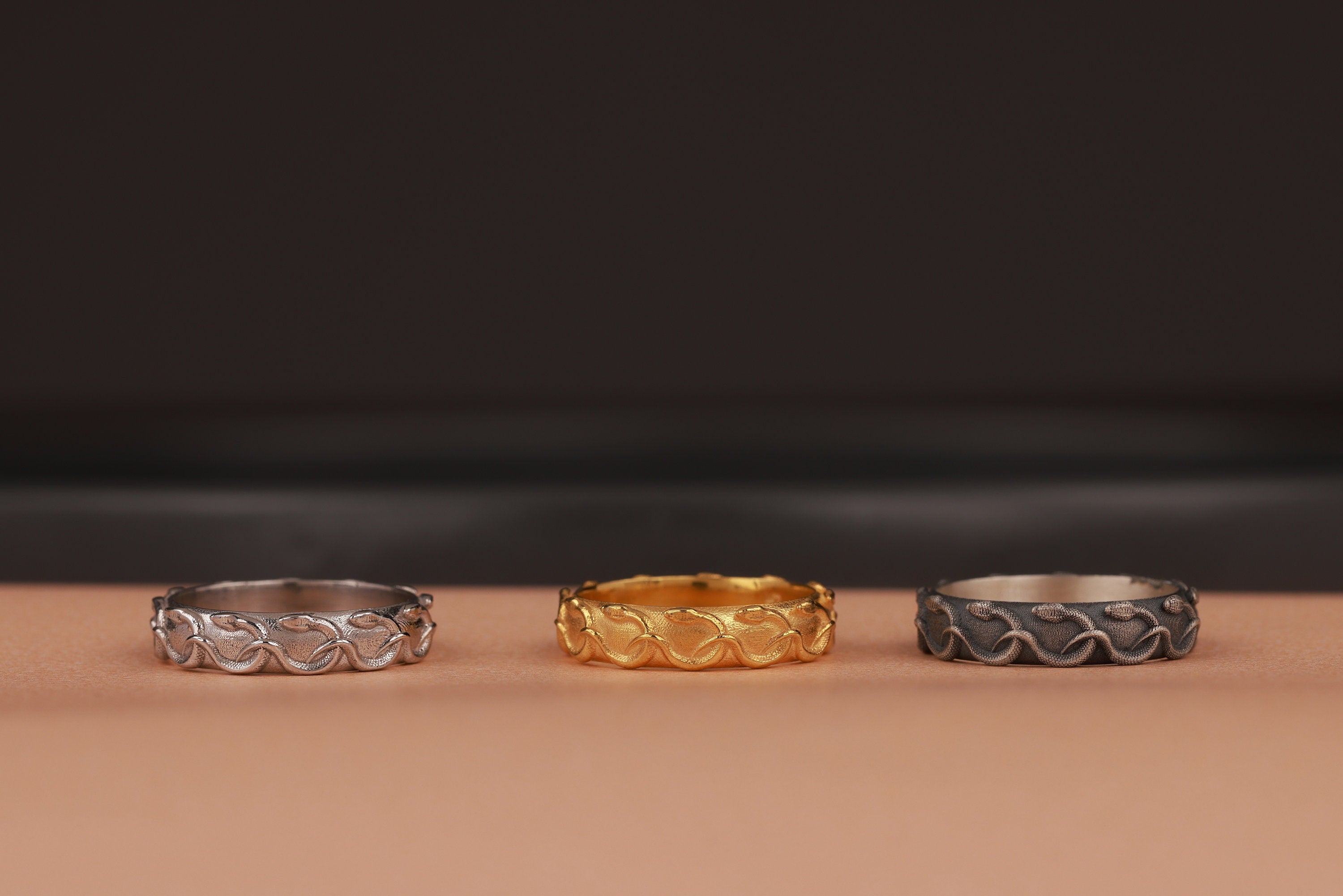 Three rings in silver, gold, and black on a brown surface with a dark background