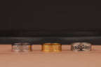 Three tree of life rings, two silver and one gold, with tree designs on a dark background