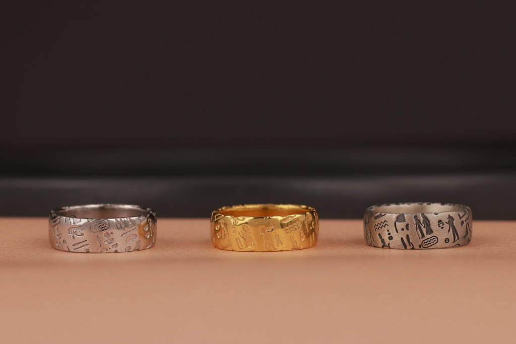 Three rings, two silver and one gold, on a beige surface with a dark background