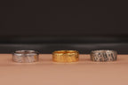 Three rings, two silver and one gold, on a beige surface with a dark background