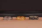 Three rings, two silver and one gold, on a brown surface with a dark background