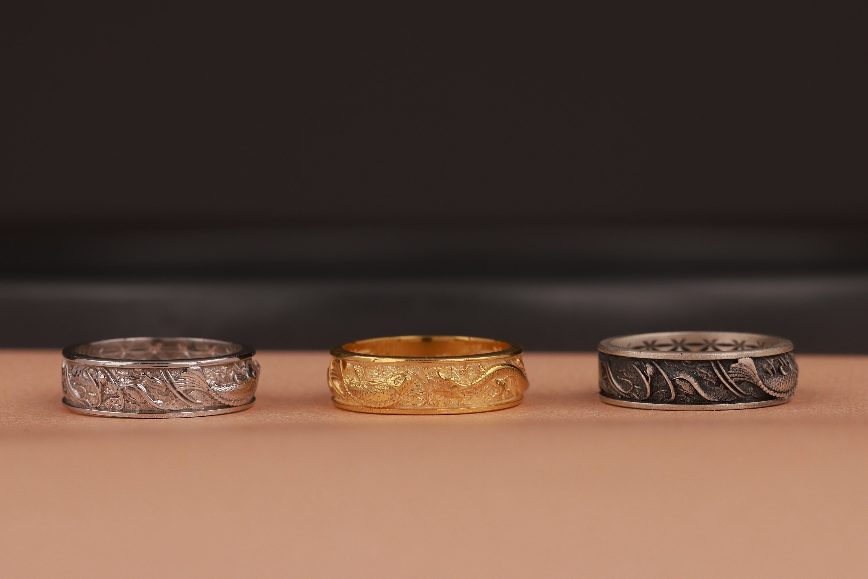 Three rings, two silver and one gold, on a brown surface with a dark background