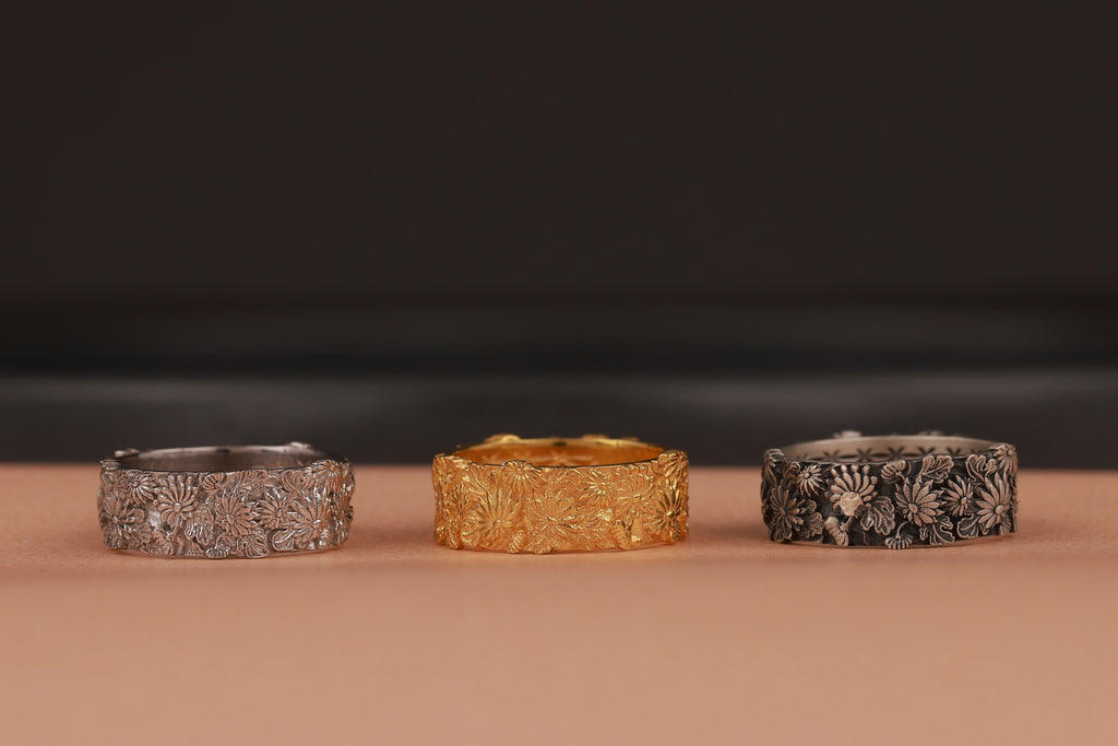 Three rings in silver, gold, and black on a brown surface with a dark background