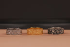 Three rings in silver, gold, and black on a brown surface with a dark background