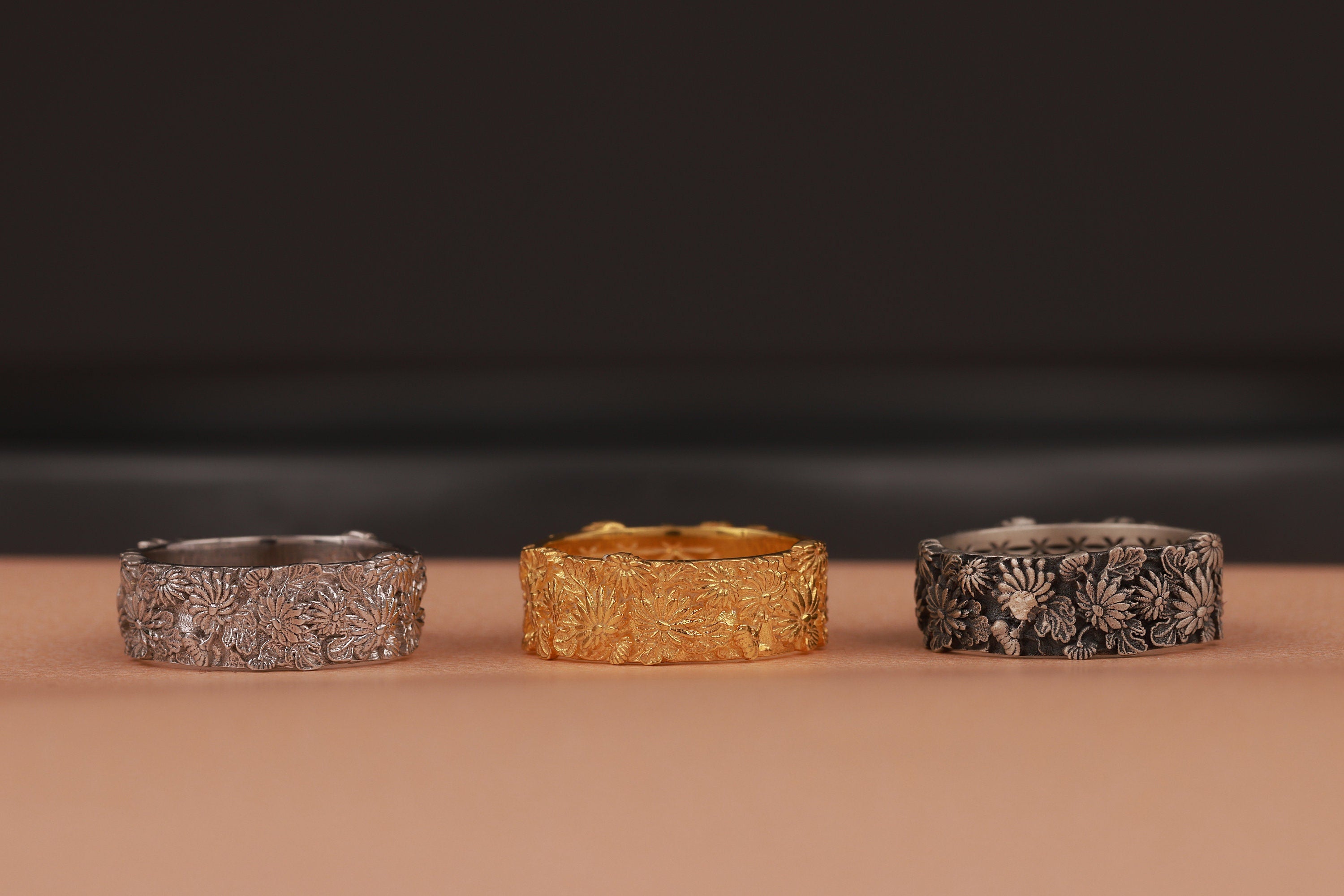 Three rings in silver, gold, and black on a brown surface with a dark background